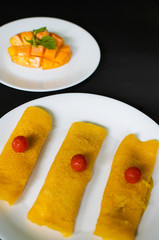 Mango crêpe an Indian dessert dish decorated with raw mango in the background on black surface