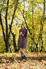 Fashion woman. Smiling girl in fur coat posin in autumn park with trees and ivy