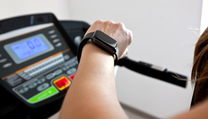 The woman is running on treadmill at home and looking on her smartwatch on her hand
