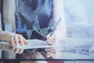 A woman hands writing information about stock market in notepad. Forex chart holograms in front. Concept of research.