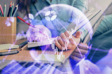 A woman hands writing information about stock market in notepad. Forex chart holograms in front....