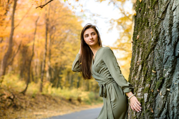 Portrait of brunette woman in green dress posing in autumn park
