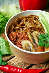 Vegetarian bowl with buckwheat noodles, fried banana, cucumber and kimchi on a wooden tray in a composition with fresh vegetables.