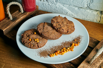 Homemade chocolate cookies with sea buckthorn on a white plate on a wooden background