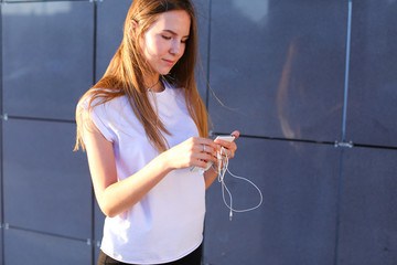 One young female woman unravels headphones for listening to music, talk on Skype, holds in hands...