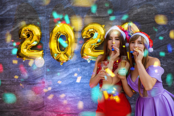 Happy girls with champagne and golden air balloons in elegant evening dresses celebrating new year