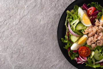 Salad with tuna, egg and vegetables on black plate and gray background. Top view. Copy space