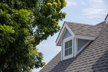 Roof shingles with garret house on top of the house among a lot of trees. dark asphalt tiles on the roof background © Rattanachat