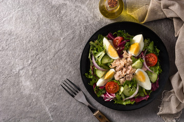 Salad with tuna, egg and vegetables on black plate and gray background. Top view. Copy space