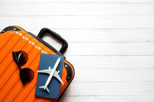 Flat lay holiday planing and traveler concept on white wooden background with passport and plane is on orange suitcase, sunglasses, Top view with copy space