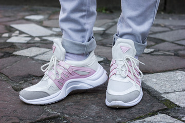 Fototapeta na wymiar beautiful white sneakers with gray and pink closeup on a female leg in gray jeans on a background of street tile