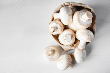 Mushrooms champignons in paper bag on a white wooden table. Place for text or advertising. Top view