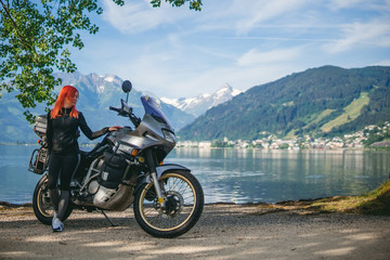 Pretty women is standing with traveler motorcycle. Vacation and hobby concept, jorney on two wheels. Sunny summer day in the Alpine mountains. Zell am see lake on background Austria. Copy space