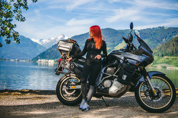 Fototapeta na wymiar Pretty women is standing with traveler motorcycle. Vacation and hobby concept, jorney on two wheels. Sunny summer day in the Alpine mountains. Zell am see lake on background Austria. Copy space