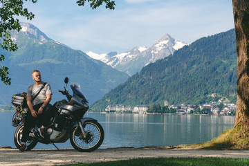 Biker standing with traveler motorcycle. Copy scpace, Vacation and hobby concept, adventure on two wheels. Sunny summer day in the Alpine mountains. Zell am see lake on background Austria.