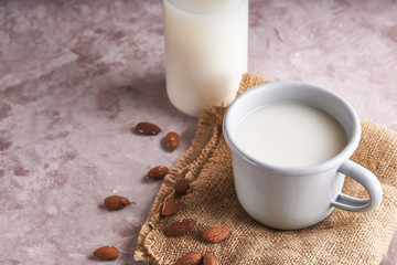 Homemade almond milk in a cup and bottle, almond kernels on rustic background. Alternative food and drink. Copy space