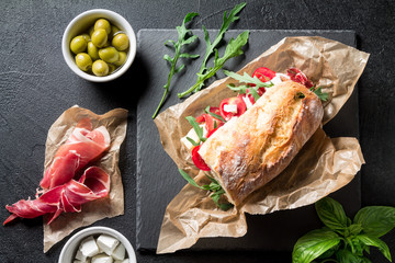 Sandwich with jamon, cheese, tomatoes and arugula on a black background
