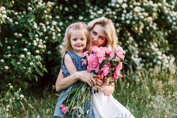 Mom with cute little daughter with flowers outside at the sunset. Concept of happy motherhood