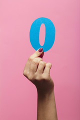 female hands showing number zero as part of date of new year 2020, cardboard figure on a colored...