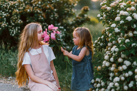 two qute sisters with peonies. Concept of happy family and love between sisters