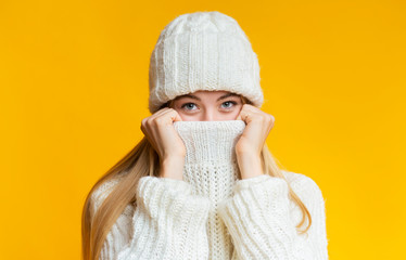 Blonde girl in winter hat covering her face with sweater