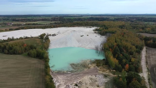 Aerial view of open pit kaolin clay mine (kaolinite quarry) with turquoise pool of water surrounded by autumn landscape with colorful trees - landscape panorama of Poland from above, Europe