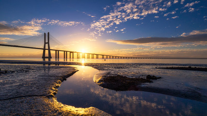 Obraz premium Vasco da Gama bridge at sunrise in Lisbon, Portugal. Vasco da Gama Bridge is a cable-stayed bridge flanked by viaducts and rangeviews that spans the Tagus River in Parque das Nações in Lisbon.