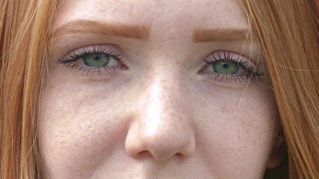 Super closeup of woman's face with green eyes, freckles and red hair, static shot