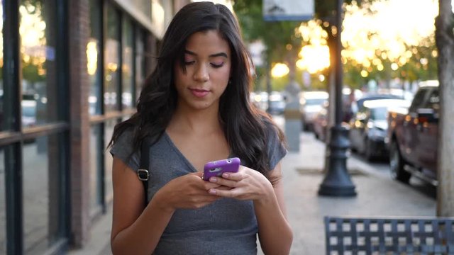 A hispanic woman walking on urban city streets texting a message on her smart phone SLOW MOTION.