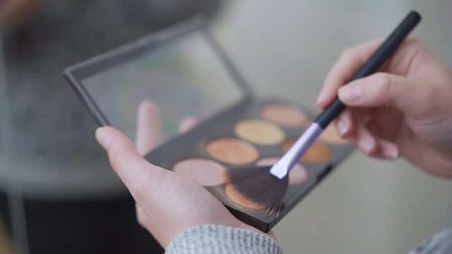 Woman's hands holding a palette of illuminator powder and make up with a brush