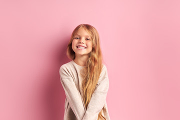 Portrait of positive cheerful girl cutely smiling at camera, girl with long golden hair in white blouse. Pink background - Powered by Adobe