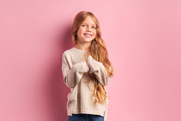 Portrait of positive cheerful girl cutely smiling at camera, girl with long golden hair in white blouse. Pink background