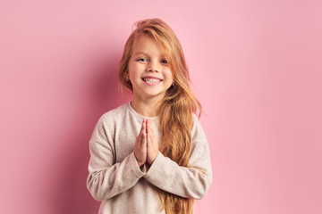 Toothy smile of little girl in white blouse holding hands together isolated on pink background