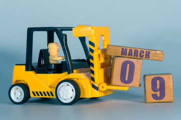 march 9th. Day 9 of month, Construction or warehouse calendar. Yellow toy forklift load wood cubes...