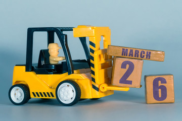 march 26th. Day 26 of month, Construction or warehouse calendar. Yellow toy forklift load wood cubes with date. Work planning and time management. spring month, day of the year concept