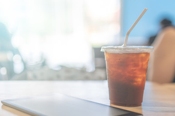 a plastic cup of ice americano coffee and table on wooden table in cafe
