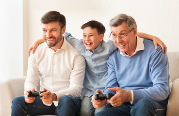 Elderly Man, Mature Son And Grandson Playing Videogame At Home