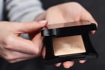 Woman's beauty blogger hands holding professional hi-end tone powder cosmetics with blurred grey...