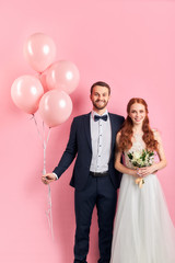 caucasian wedding couple posing together isolated over pink background. Handsome man in tuxedo...