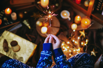  The atmosphere of the New Year or Christmas, a girl in blue festive pajamas holds a burning sparkler in her hands