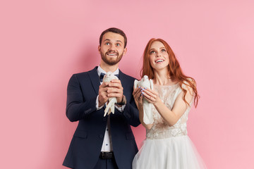 Beautiful woman with red hair wearing white wedding dress stand together with fiance in suit and holding doves in hands, preparing to let them out of hands