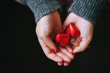New Year's atmosphere, Christmas, a girl in a red sweater holds decoration toys - two hearts in her hands