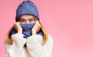 Enigmatic winter girl hiding from cold over pink background