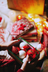 Celebrating New Year and Christmas at home, a girl wraps gifts and holds  decorations for christmas tree in a cozy atmosphere