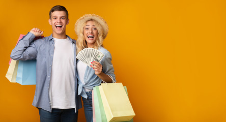 Fototapeta na wymiar Excited Young Couple Holding Paper Bags And Bunch Of Dollars