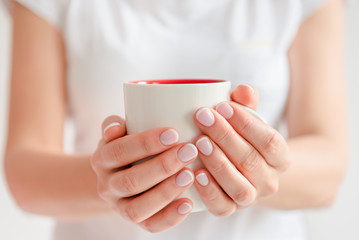 Woman in a white t-shirt holds morning coffee in a white ceramic cup. Christmas concept. Front view