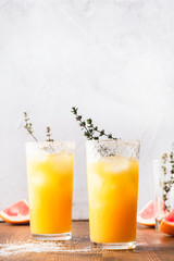 Citrus juice with ice in glass glasses and slices of fruits on a wooden table, light grey background, front view.