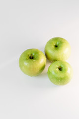 Fresh green apples with water droplets on a white glossy kitchen table. Tasty bright juicy fruits. Healthy eating. Isolated object.