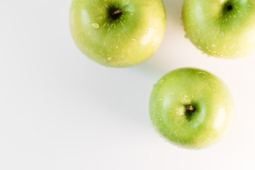 Fresh green apples with water droplets on a white glossy kitchen table. Tasty bright juicy fruits. Healthy eating. Isolated object.