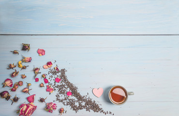 Tea time concept. One cup of tea, dry tea and rose buds and flowers on the blue paint wooden background. Copy space, flat lay